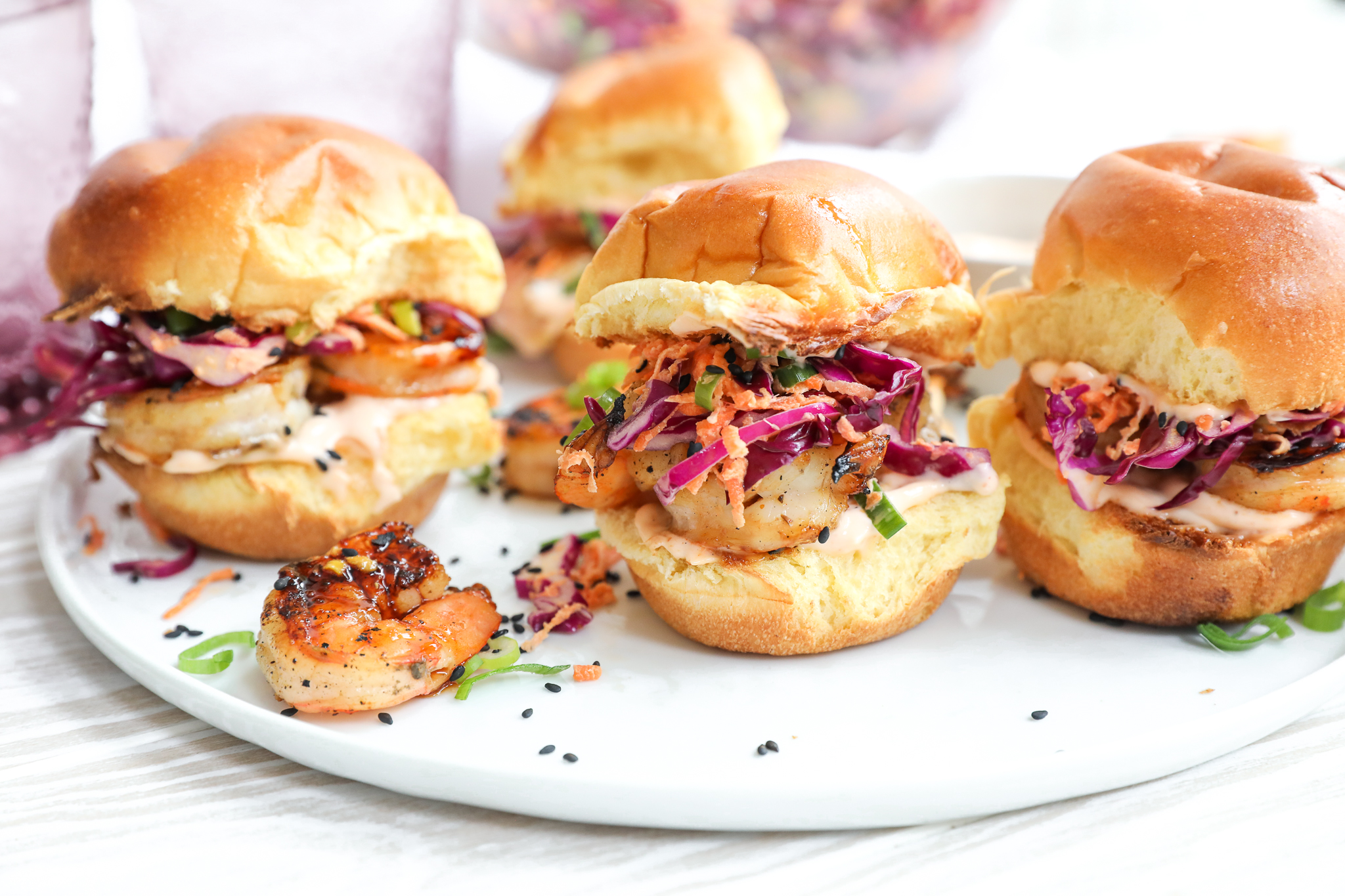 Grilled Asian Shrimp Sliders with Sesame Ginger Slaw | My Cape Cod Kitchen An image of shrimp sliders on a white plate with more sliders in the background