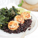 Seared scallops on black rice with kale on a white plate.