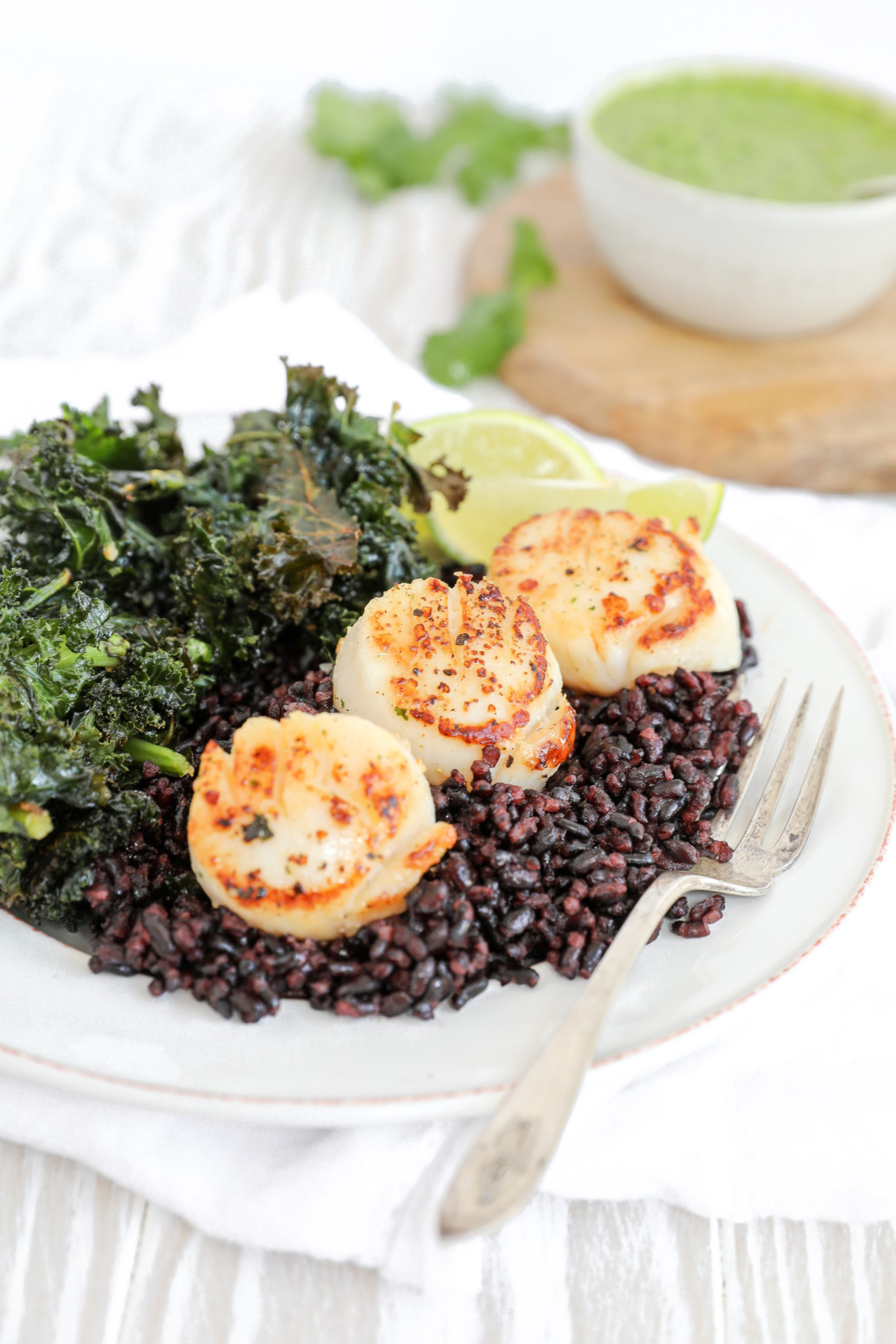 Seared scallops on black rice with kale on a white plate.