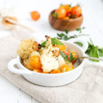 Roasted Cauliflower Caprese Casserole in a small white bowl with a bowl of tomatoes behind it.