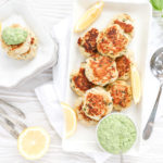 An overhead shot of crabcakes on a rectangular white plate with creamy pesto on the side.