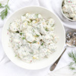 A large white bowl with creamy potato salad and a small bowl with one serving in it.
