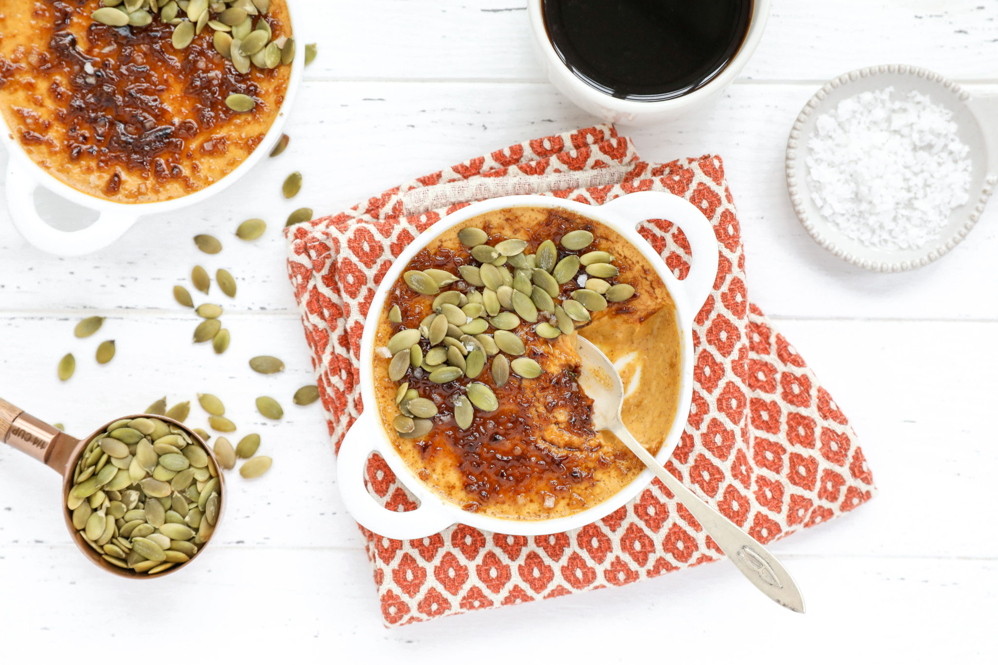 Salted Pumpkin Crème Brûlée An overhead shot of pumpkin creme brûlée in a small dish with pumpkin seeds and a spoon on a fall inspired napkin.