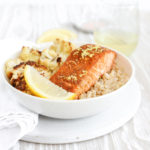 A white bowl of baked salmon with lemon zest over brown rice with cauliflower.