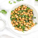 A bowl of chickpeas with fresh herbs on a white napkin next to a bowl of sea salt